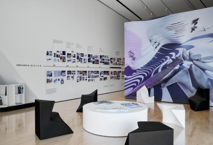 Image of exhibition with timeline of information, Zaha Hadid designed chairs, and large abstract photo mural