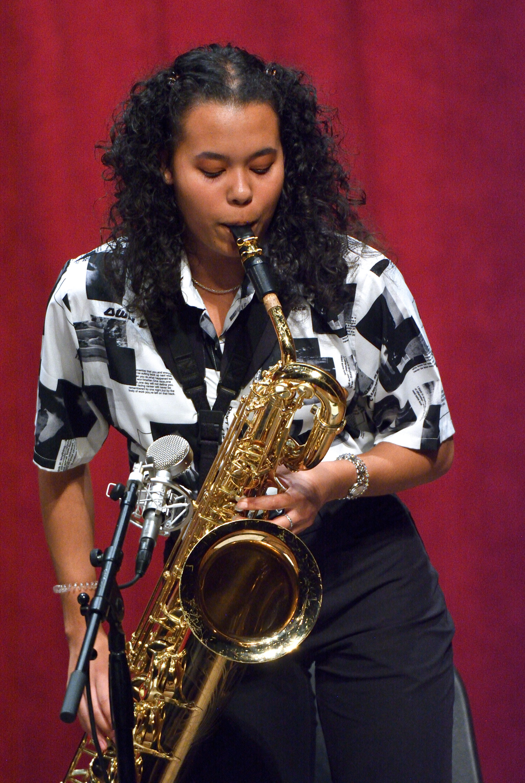 Woman with curly black hair and black and white shirt plays alto saxaphone