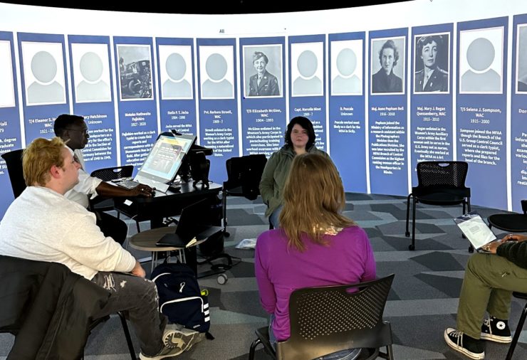 Class works in the the 360 Degree Visualization Room, surrounded by images and text related to the women they were studying