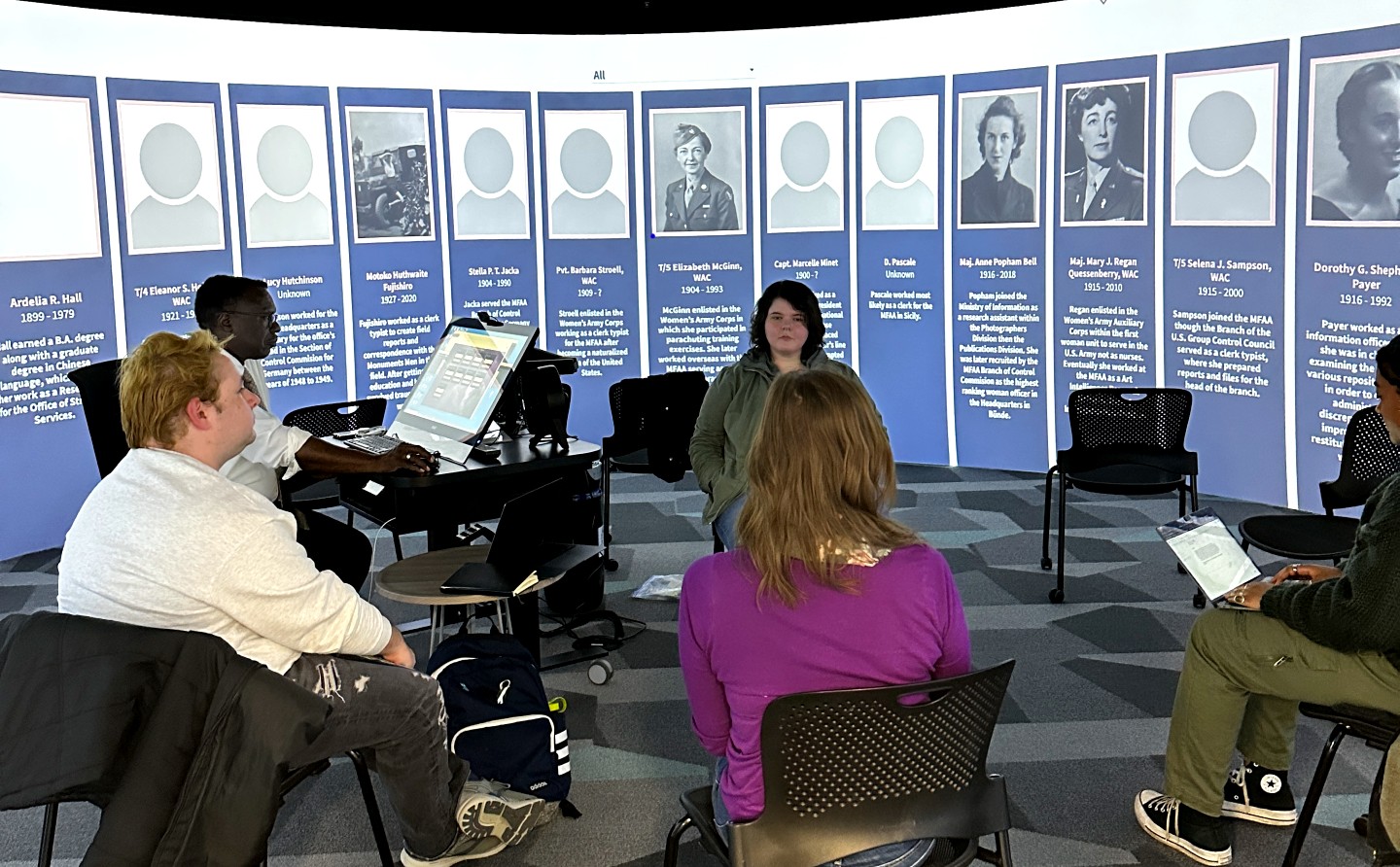 Class works in the the 360 Degree Visualization Room, surrounded by images and text related to the women they were studying