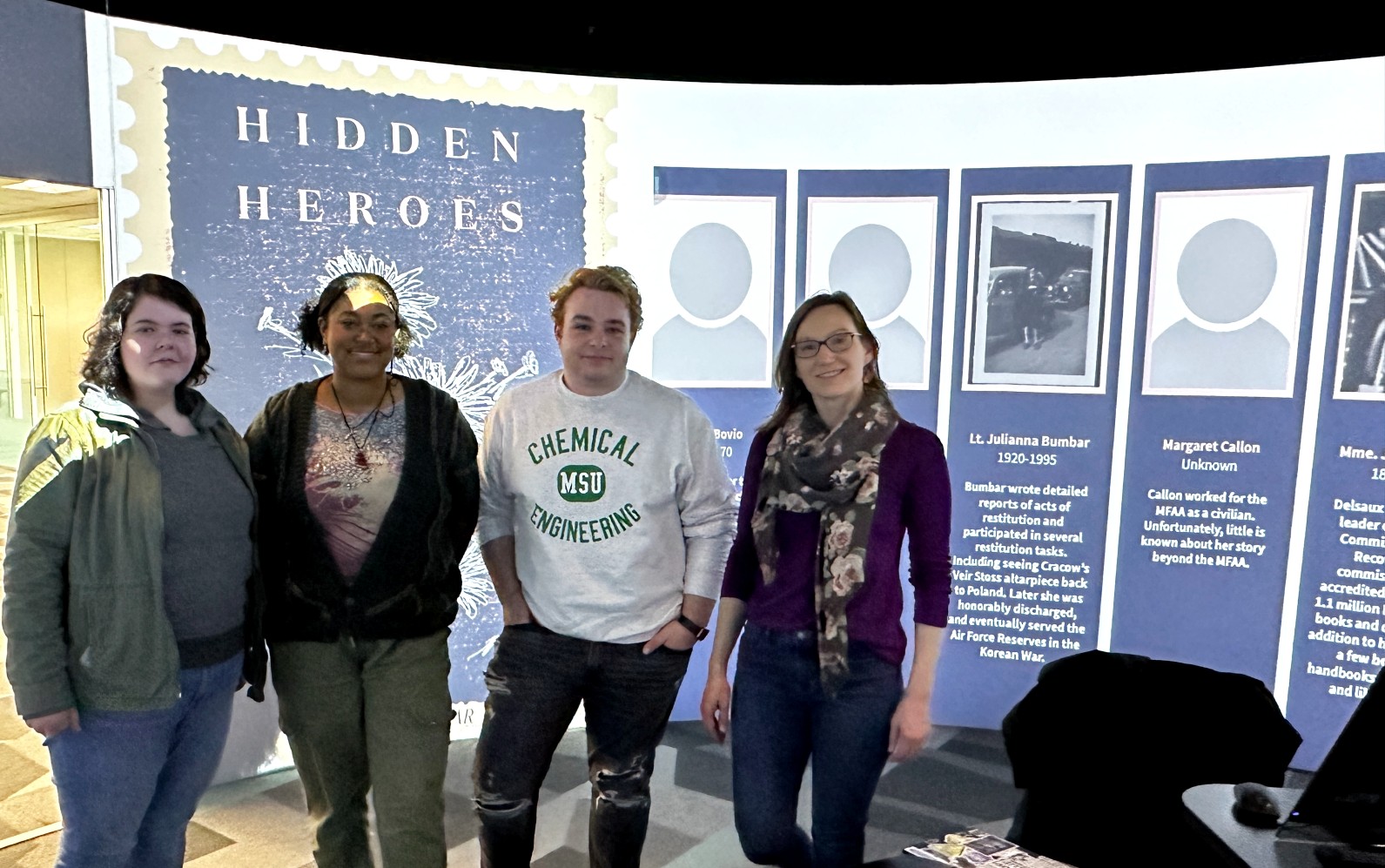 Oliviah Brown, Taylor Hughes-Barrow, Michael Griffin, and Kristen Mapes in front of the projection of their Hidden Heroes work.