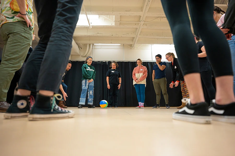 MSU theatre students in a white workshop room performing an activity in a circle around a colorful beach ball