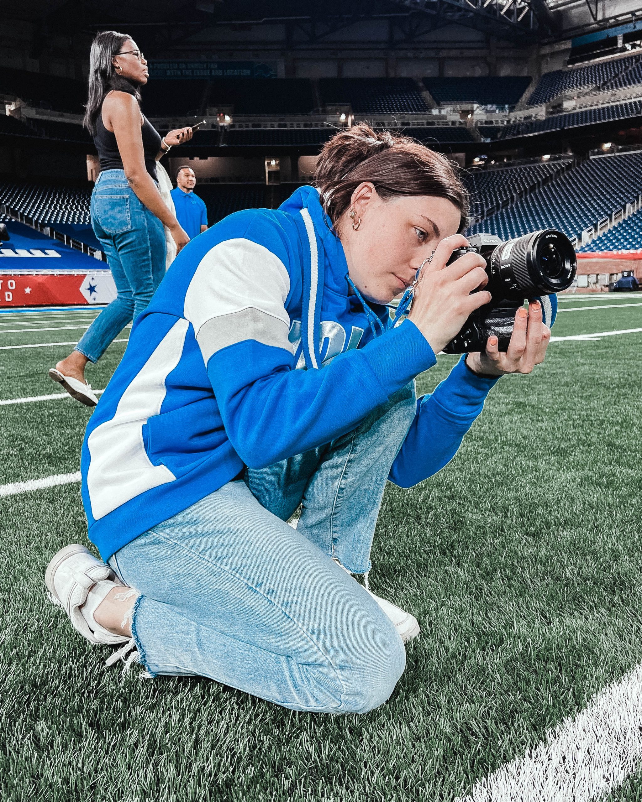 Katie Quinlan taking photos while on the field in Lions sweatshirt.