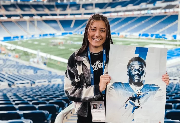 Graduate Katie Quinlan holds up a poster she designed herself at Ford Field