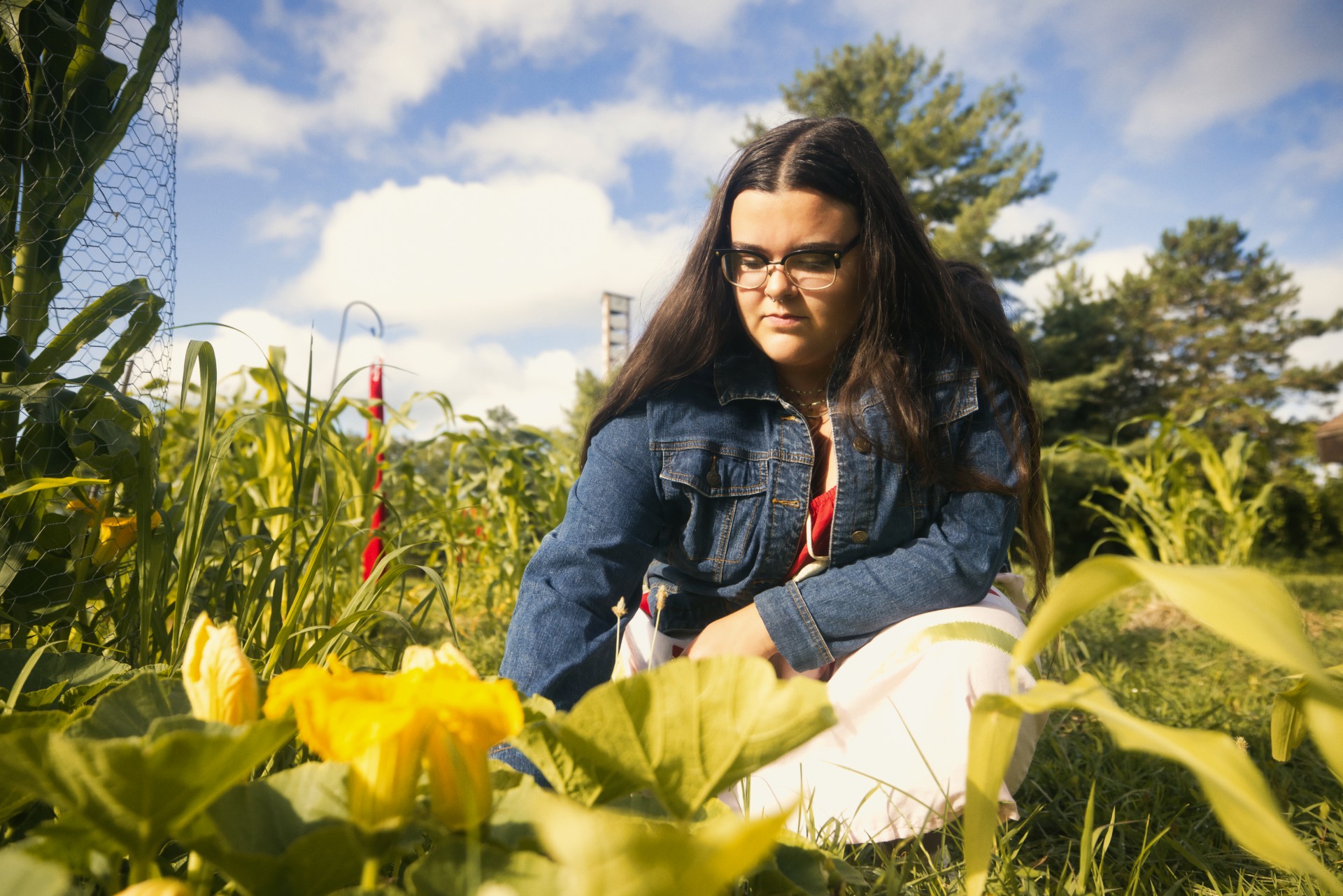 Mikayla in jean jacket leaning forward looking at yellow flowers