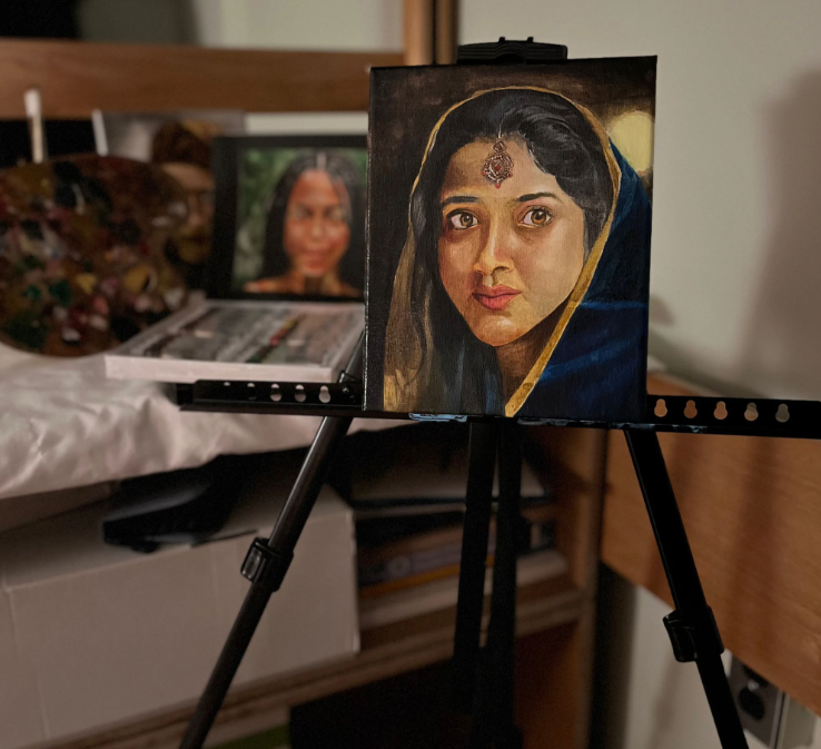 A painting of a woman in a dark blue headscarf on an easel, with art supplies in the background.