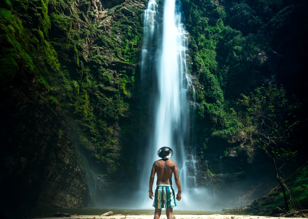 Vadu standing with back facing the camera, looking at a waterfall.