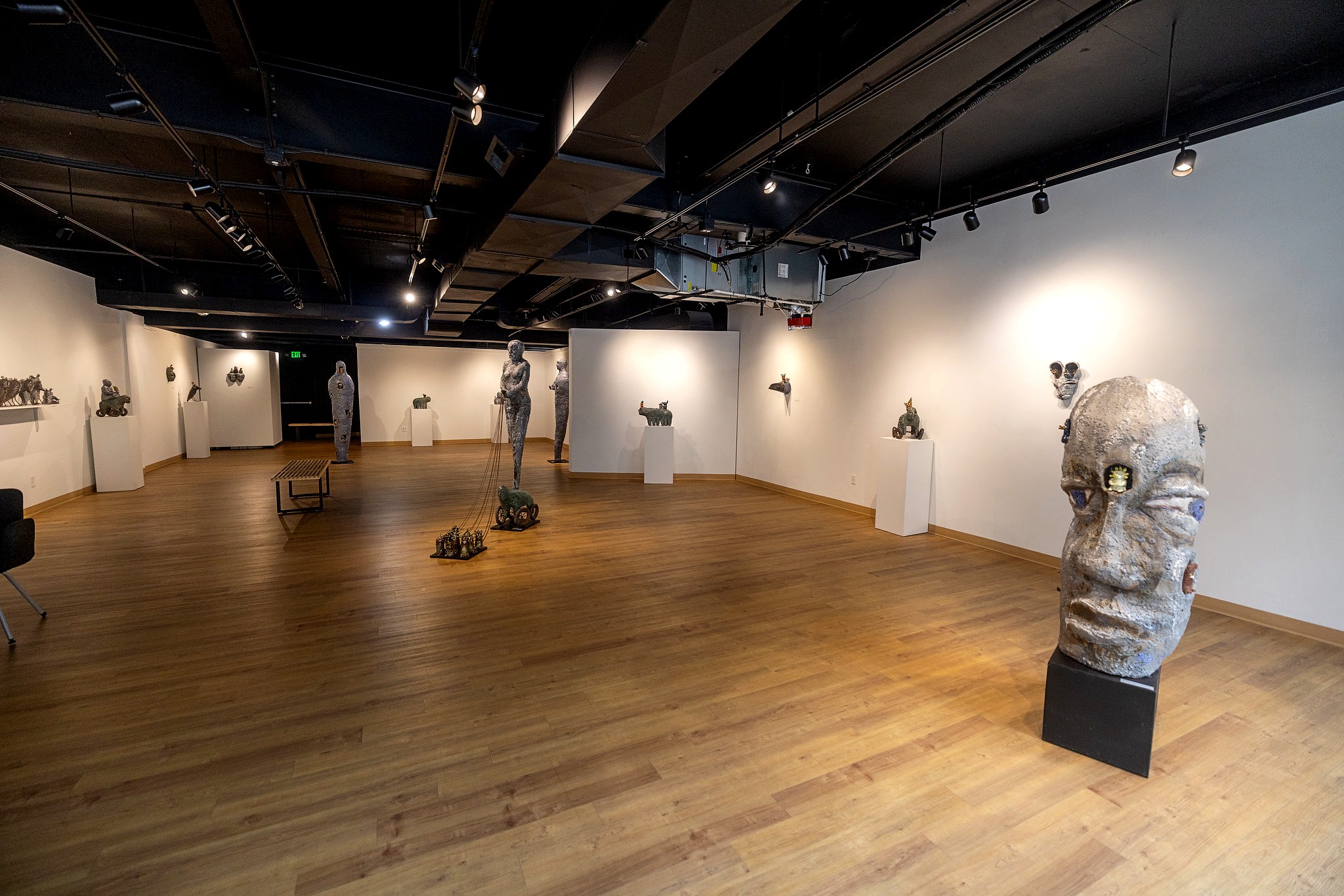A picture of an art gallery with wooden floors and white walls displaying a variety of humanoid and animal-like ceramic sculptures.