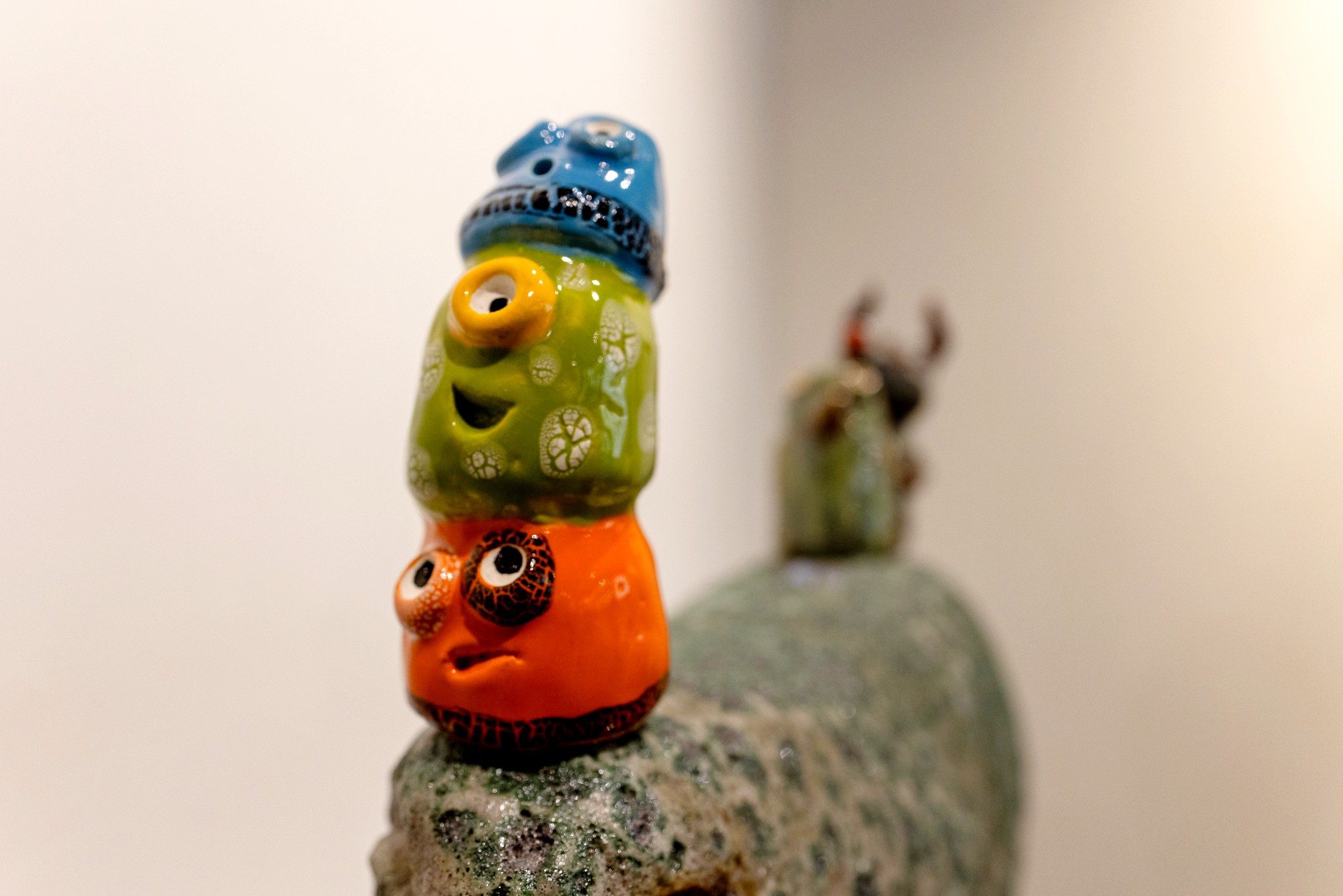 A close-up photo of three brightly colored round weird and silly faces stacked on top of each other, made from clay/ceramic.