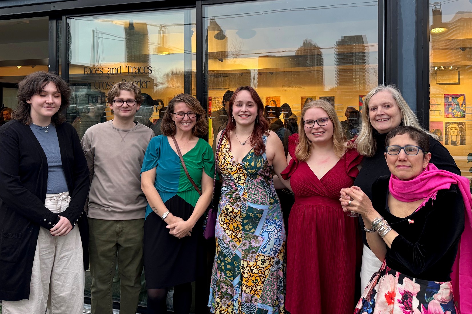 Seven people stand smiling outside a gallery with the exhibition title 