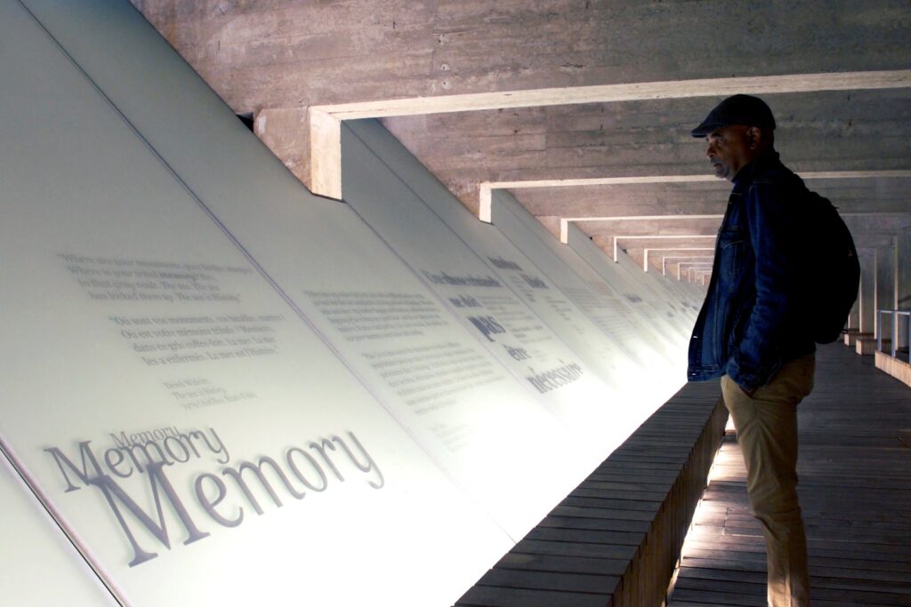 A man standing in front of a lighted board at a museum and on the board it reads