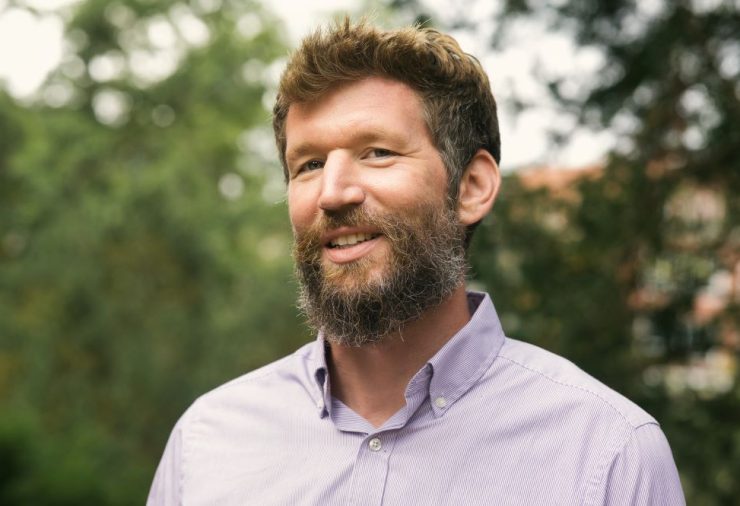 Portrait of MSU Assistant Professor Tim Conrad smiling. He's wearing a button down shirt and in the background are tree branches.