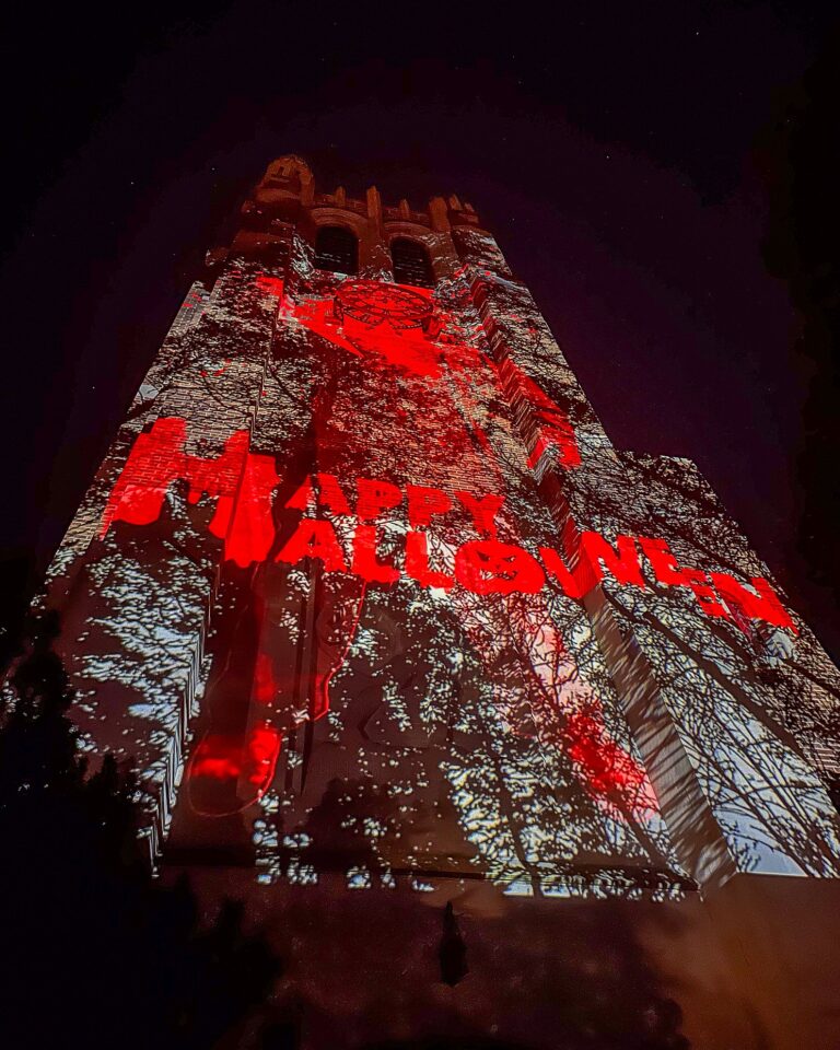 A dramatic red and white projection covers Beaumont Tower with silhouetted tree branches and bold text that reads