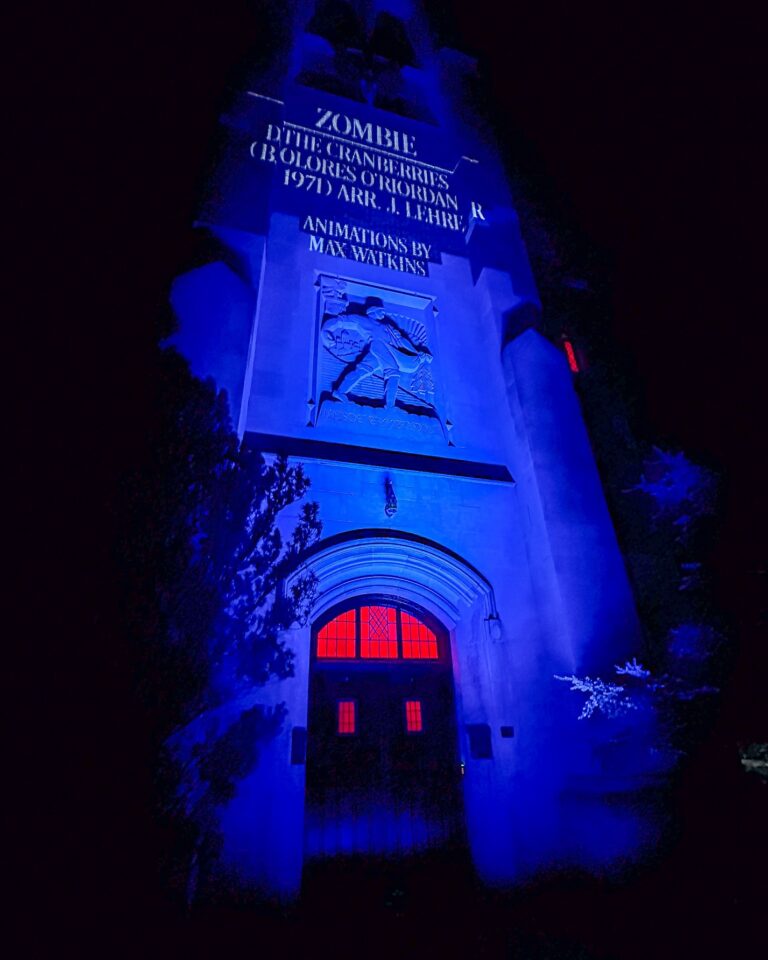 Beaumont Tower illuminated in blue light with red glowing windows. Projected text on the tower reads