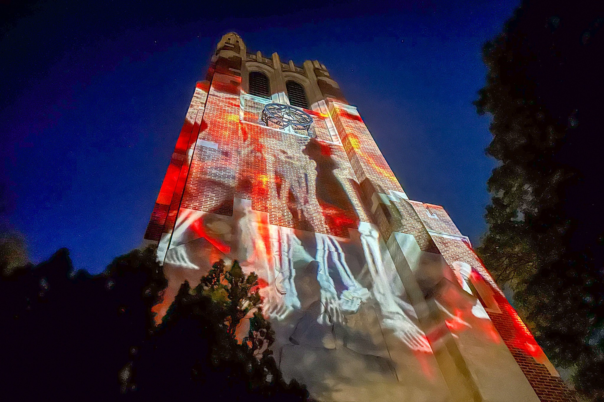 Beaumont Tower lit with vivid red and white projections depicting skeletal figures climbing up the brick facade against the evening sky.