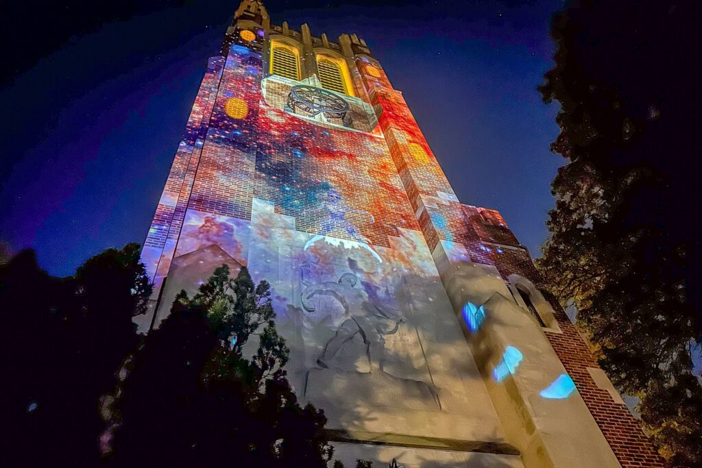 A wide view of the tower illuminated with colorful cosmic imagery-swirls of red, blue, and orange light forming a galaxy-like pattern.