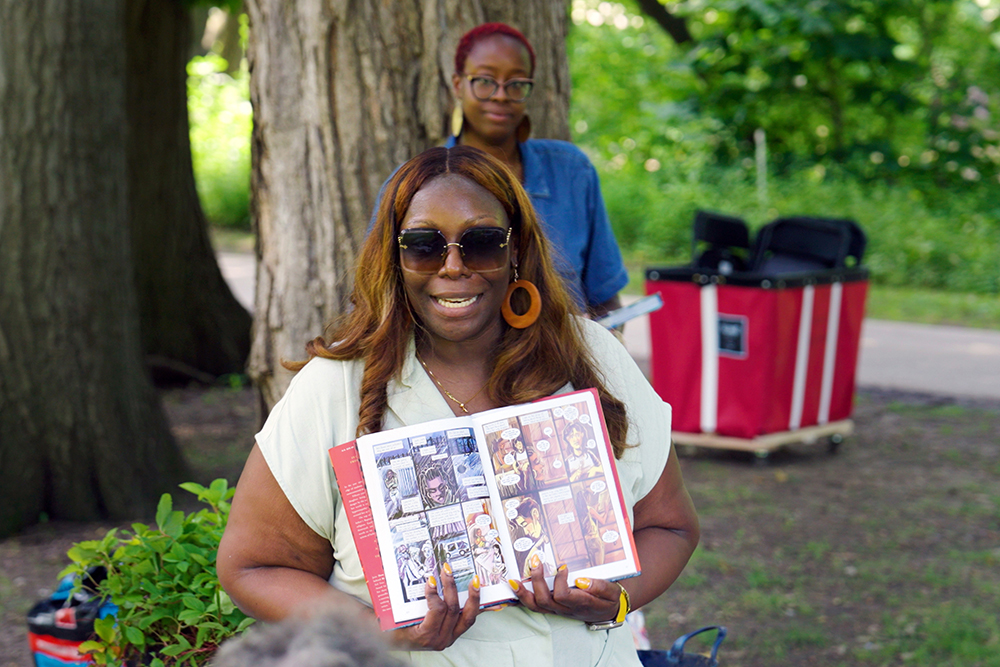 MSU Professor Kinitra Brooks holds up a graphic novel and shows off a spread of the pages. In the background is English doctoral student Cheyenne Symonette.