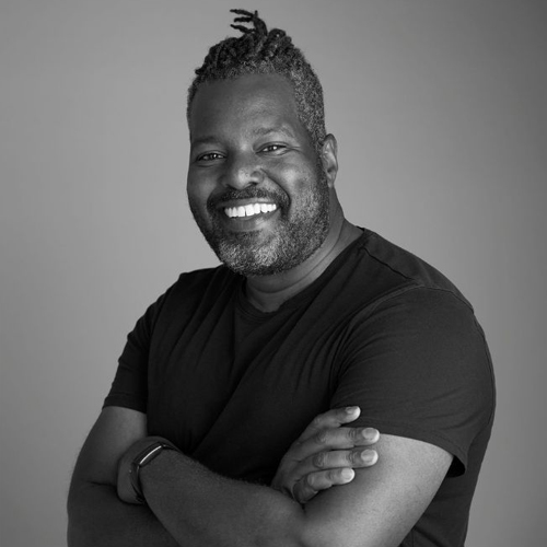 Black and white photo of man with his arms crossed in black t-shirt