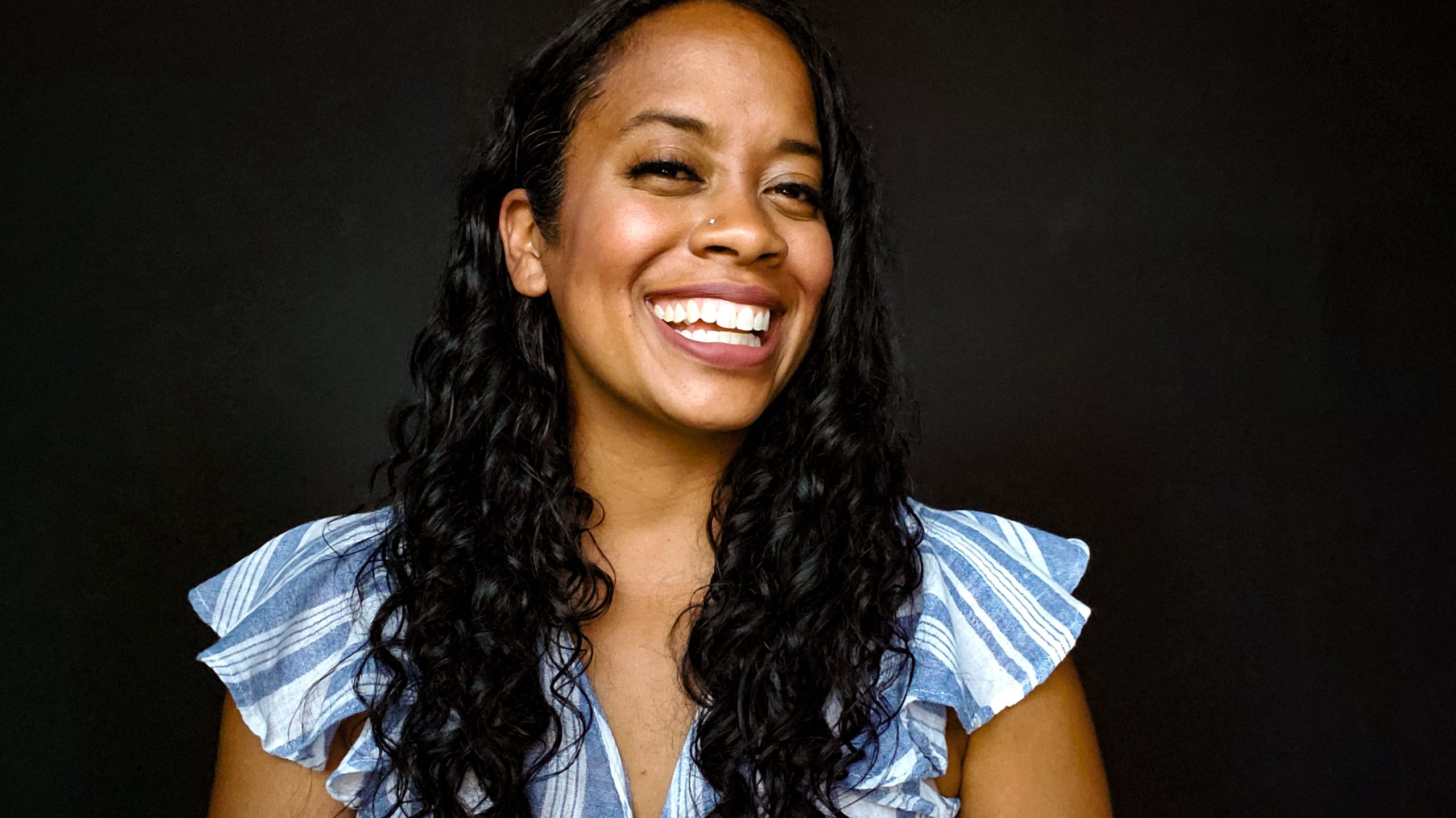 Woman with black curl hair and blue striped shirt laughs