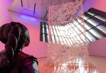 Black shea butter sculpture girl with two braids looks at large sculpted white fence