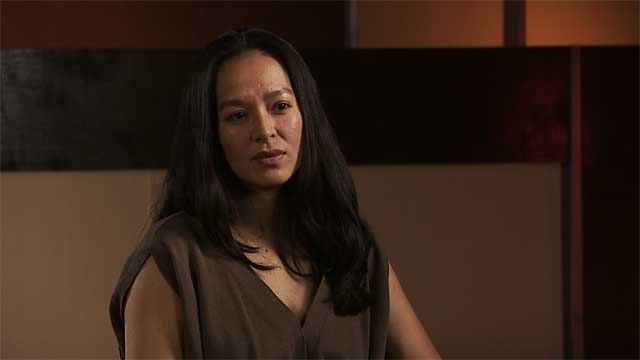 Woman in interview setting wearing brown tank top with long black hair