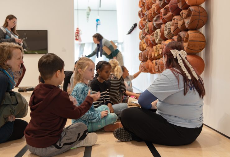 Young students gather around an educator, seated on the floor in the MSU Broad Art Museum