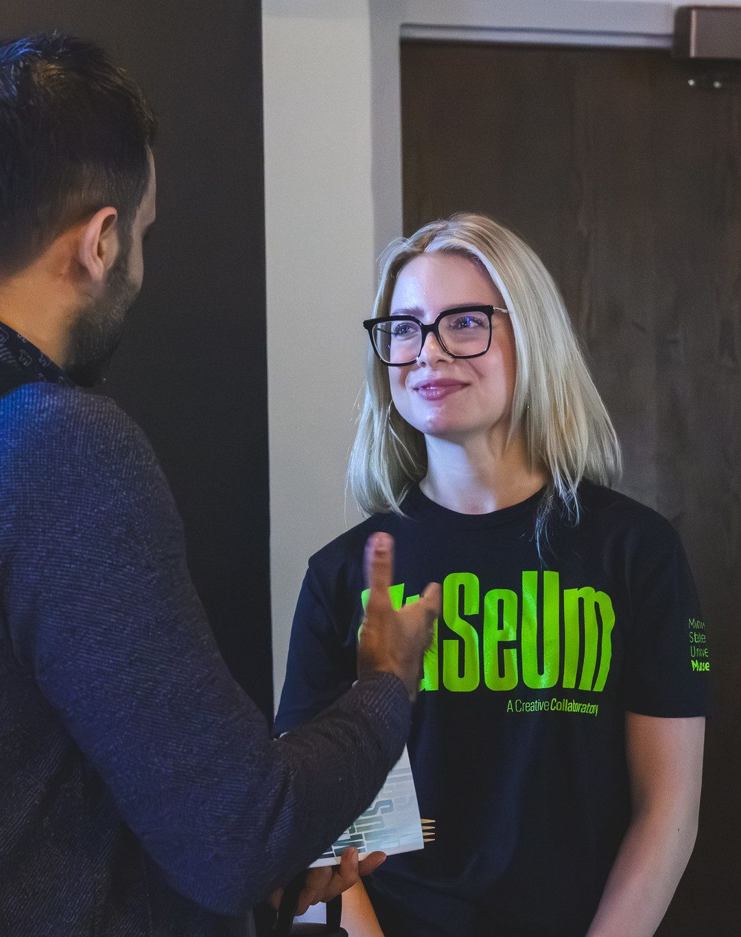 Blonde haired student employee listens to visitor, smiling