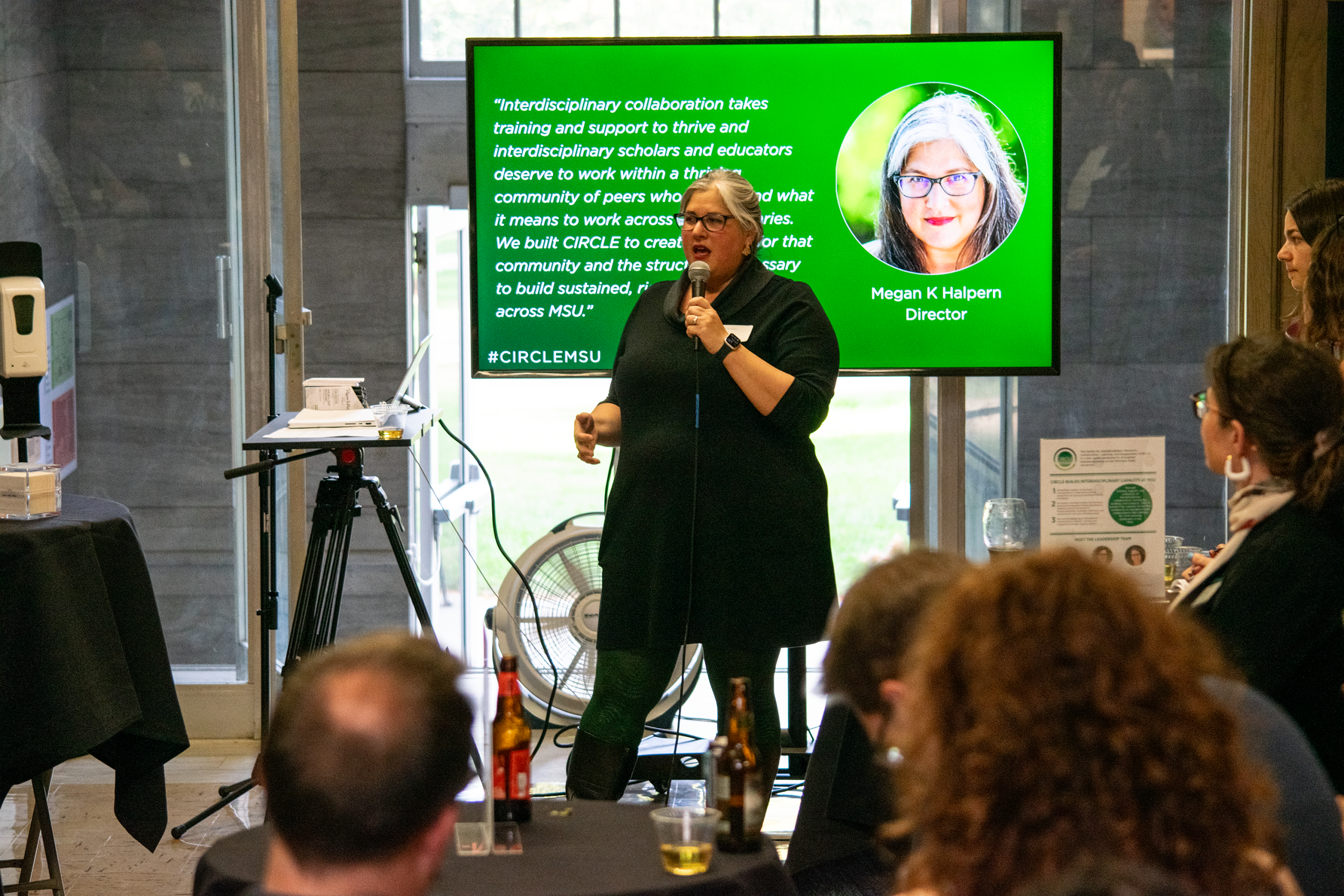A woman stands in front of a monitor with a green presentation slide explaining interdisciplinarity