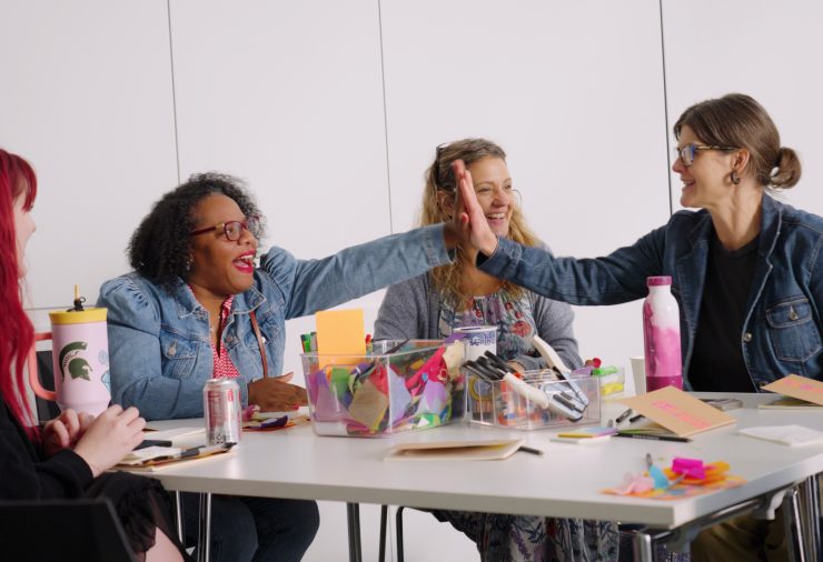 Two teachers smile and high-five each other from across a table