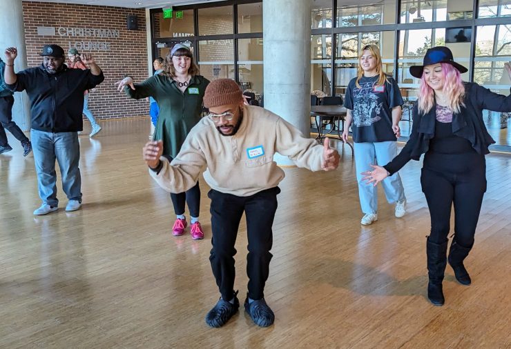 An artist in a brown beanie hat engages four participants in a dance workshop