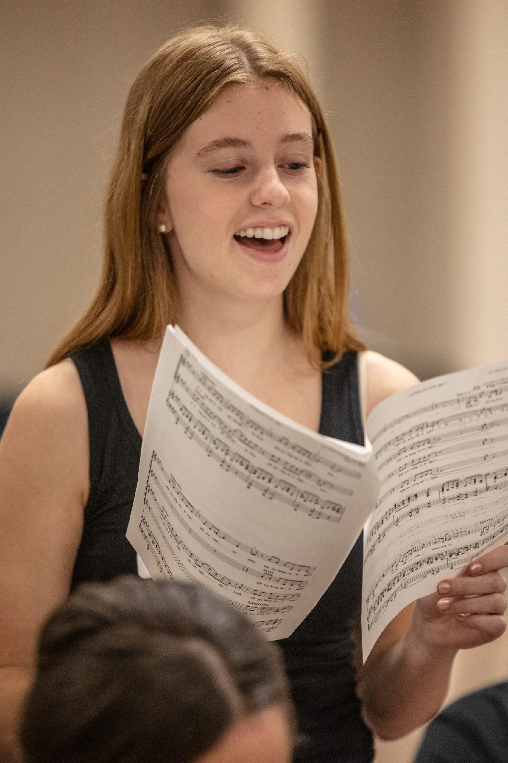 Teenaged girl with long hair sings from sheet music