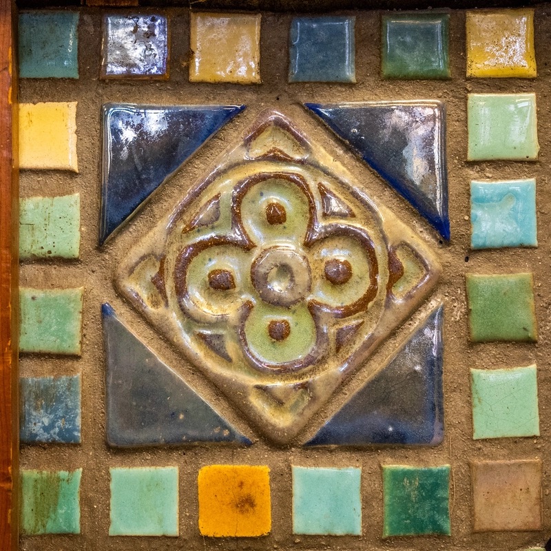 A number of small colorful tiles are arranged in the shape of a square. They are of various shapes and colors, arranged with a detailed tile in the center.