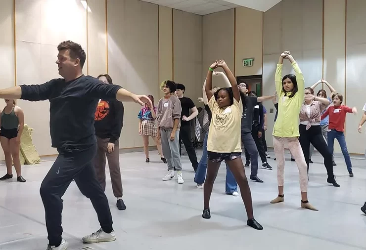 A dance instructor and several children behind him put their hands out in preparation to spin