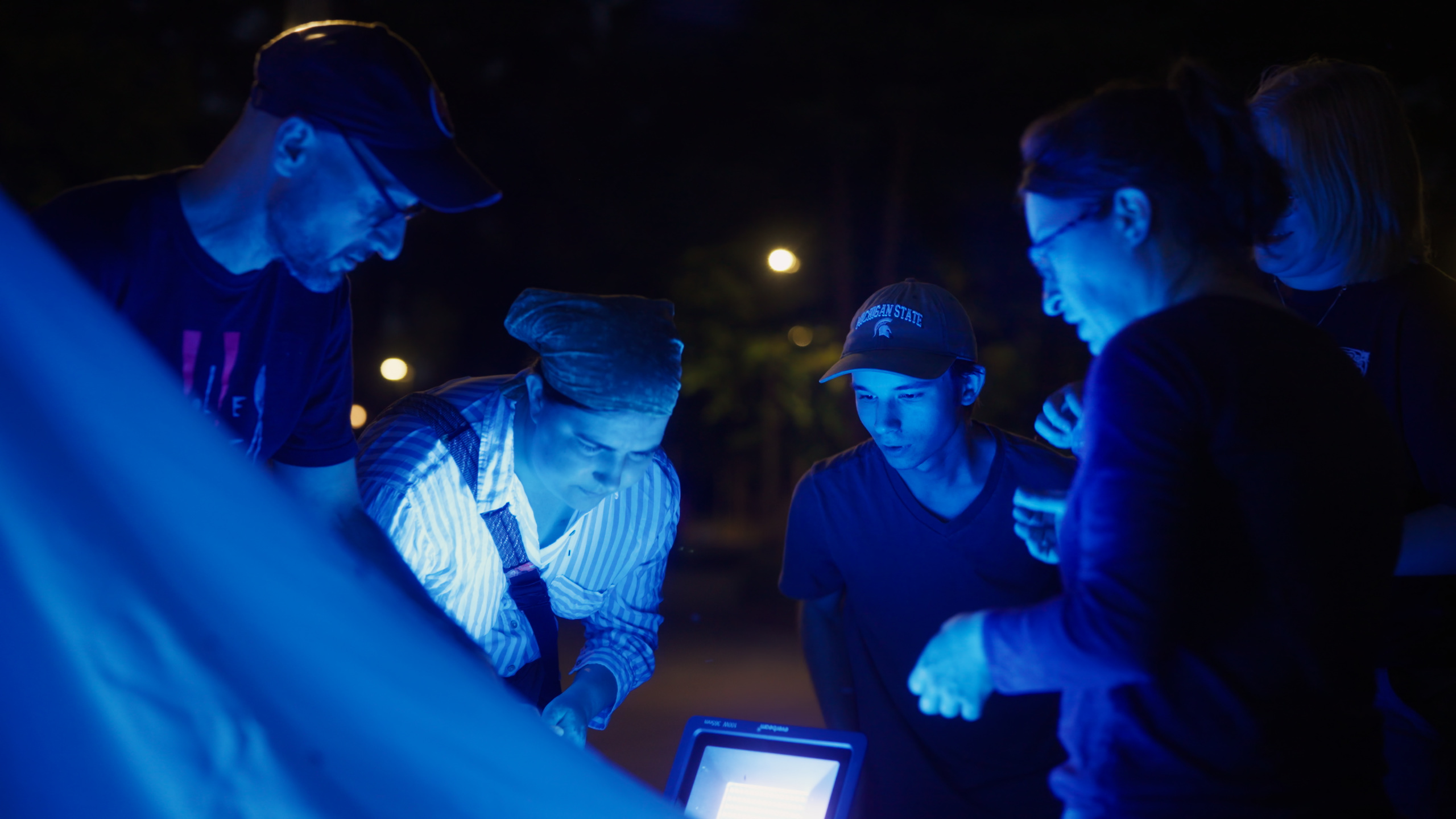Group of people huddle around a glowing blue light source for event installation.