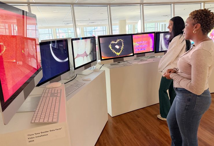 Two visitors stand before a row of iMac monitors displaying video works from the Dogs Playing Poker exhibition.
