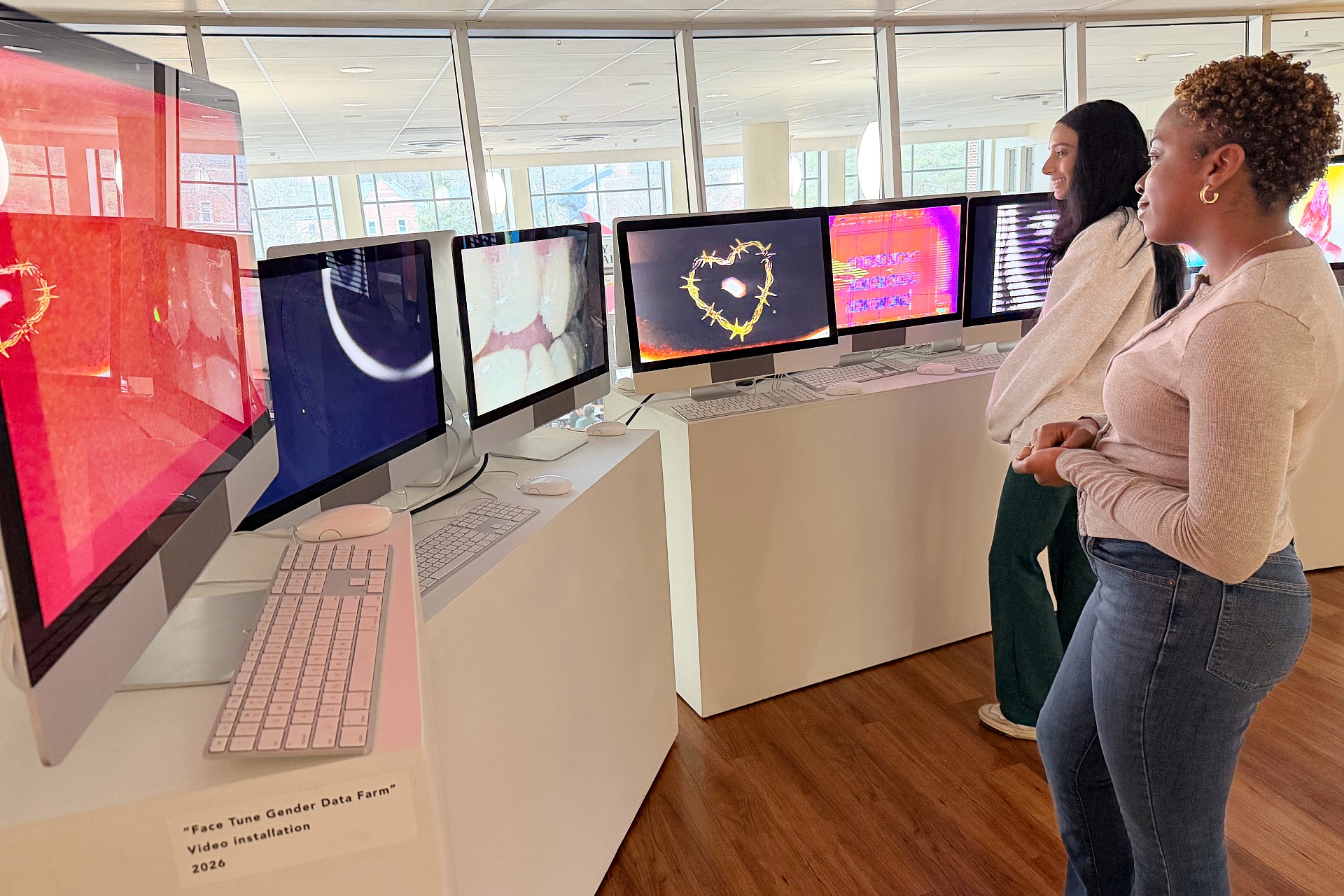 Two visitors stand before a row of iMac monitors displaying video works from the Dogs Playing Poker exhibition.