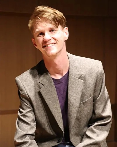 Headshot of Tyler Mazone wearing a purple shirt and a grey blazer.