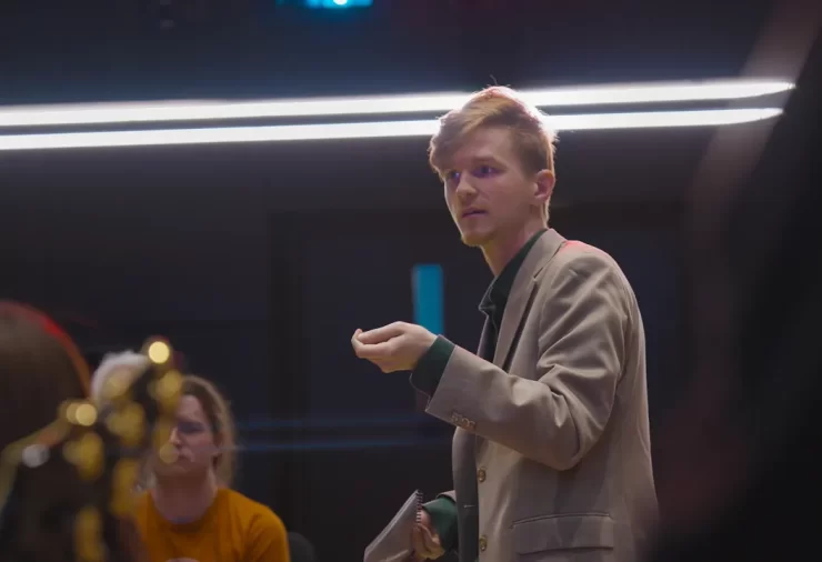 Tyler Mazone stands in a music hall, gesturing to an ensemble.