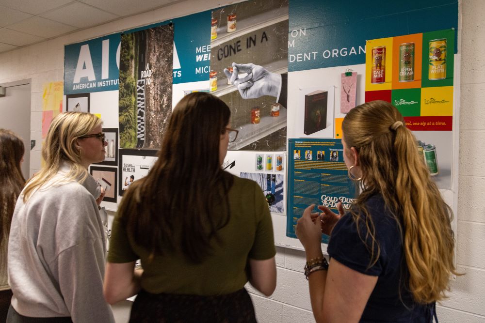 The backs of three people looking at colorful design and poster work displayed on the wall.