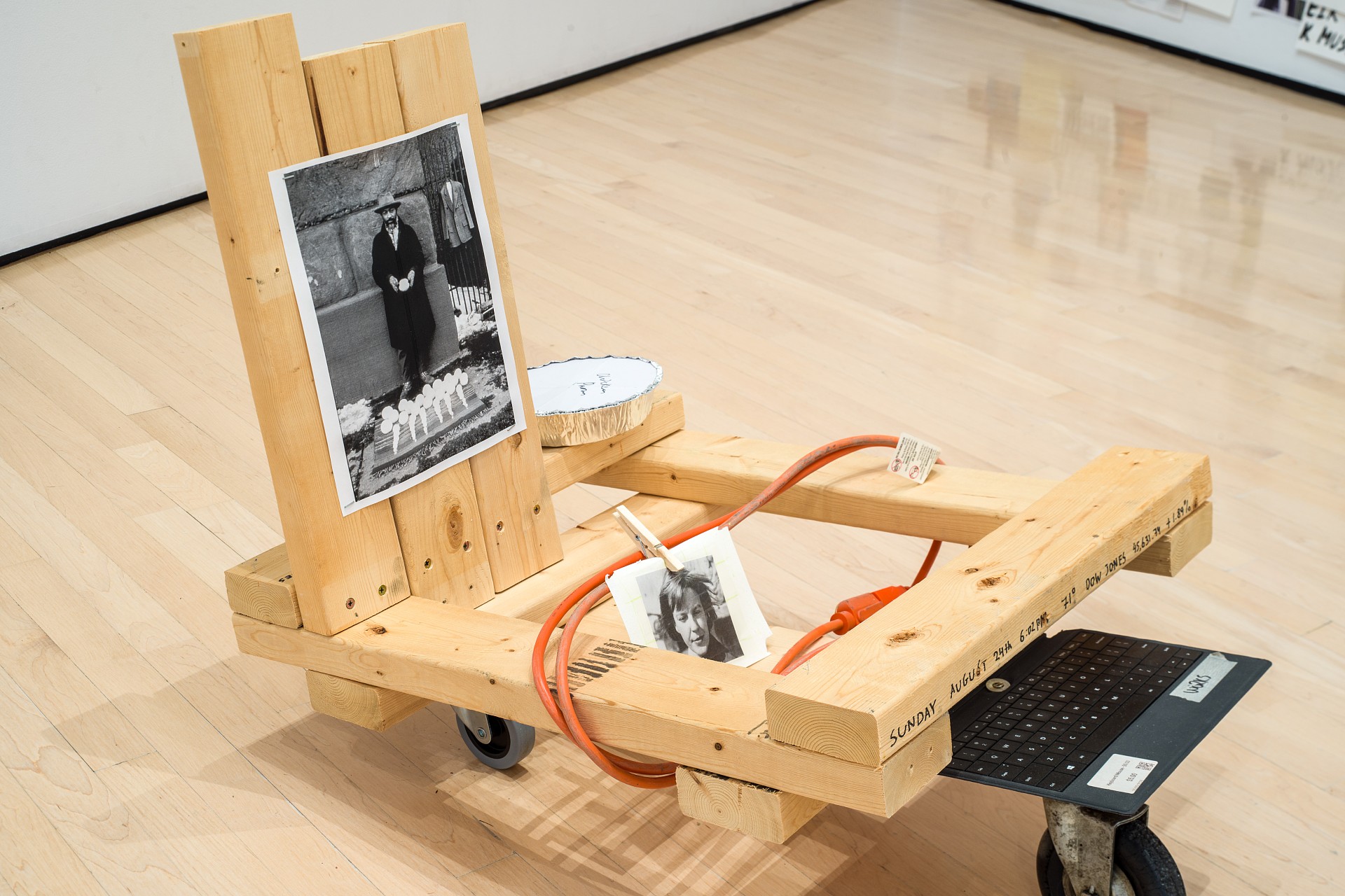 A wooden cart with black-and-white photos and a red hose on a wooden floor. The tone is artistic and thought-provoking, with a contemporary feel.
