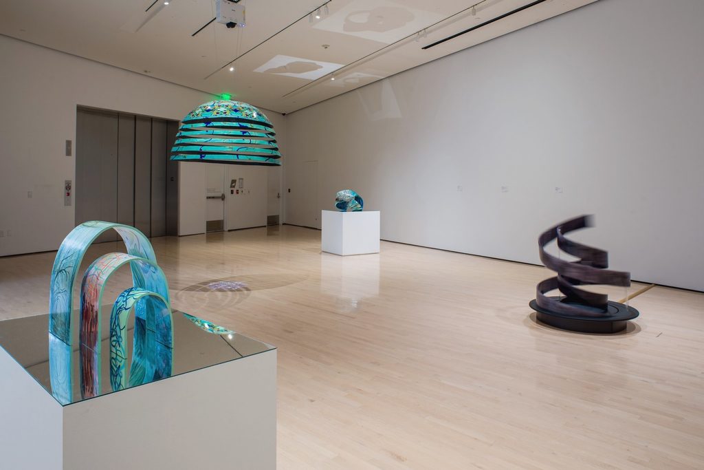 A series of three differently sized, painted sculptures on a reflective surface. Each sculpture features unique artwork.