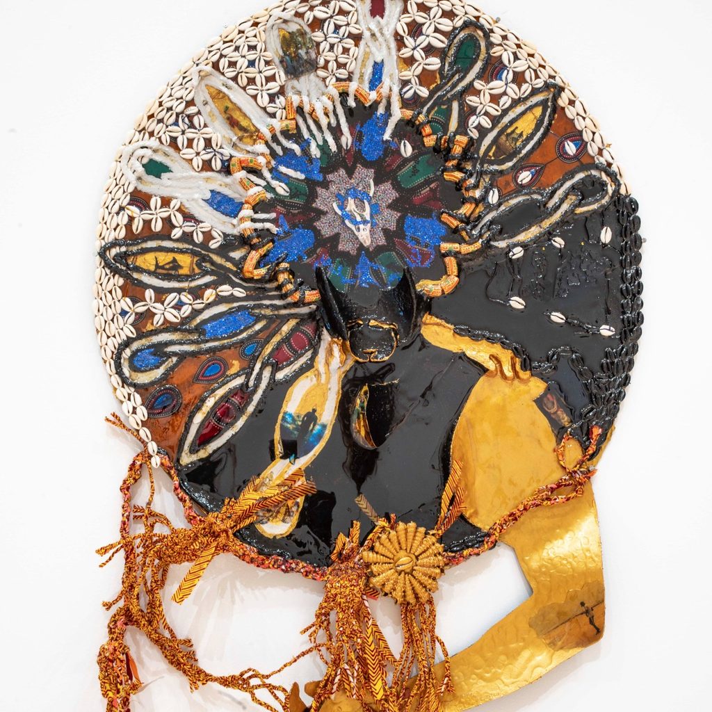 Vibrant circular artwork with intricate beadwork, gold accents, and flowing orange fringe. Features bold, colorful abstract patterns and a radiant, creative form.