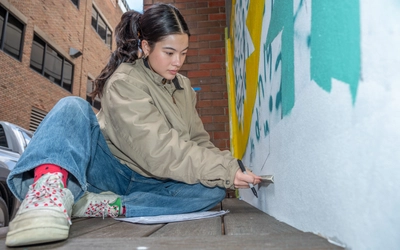 A girl sits in front of a wall holding a marker and measuring the wall with a ruler.