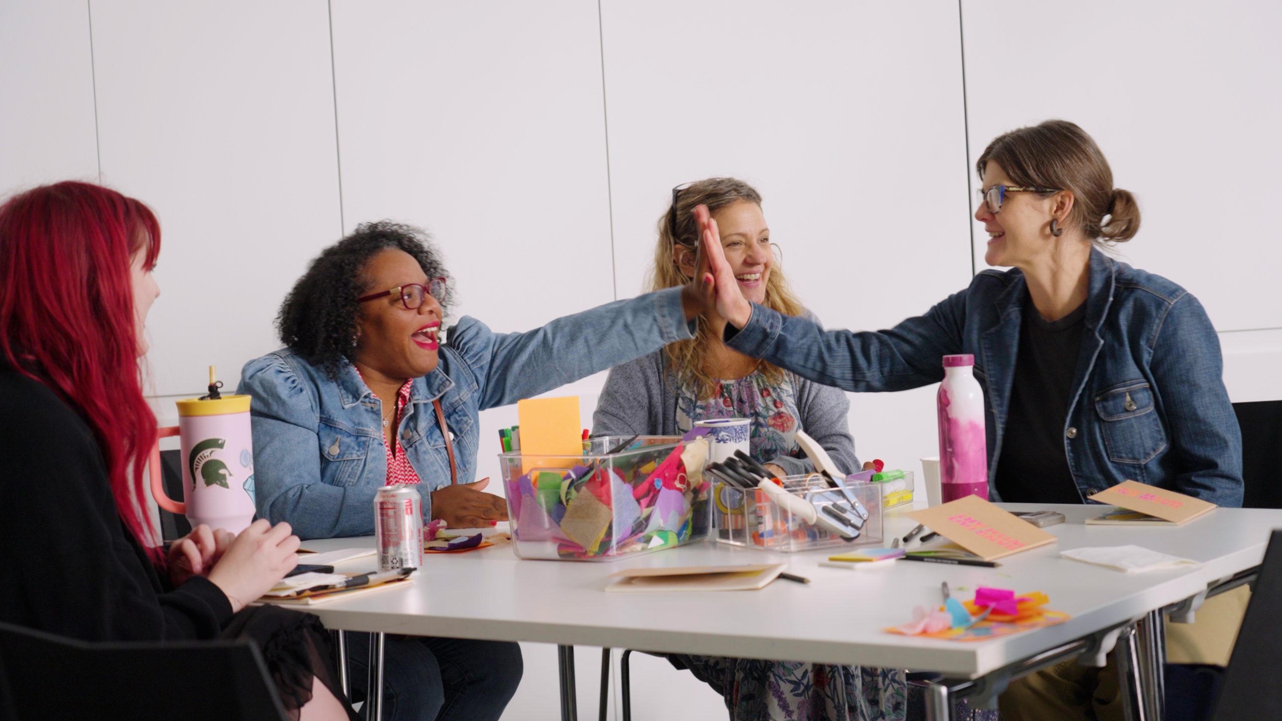 Two women educators give each other a high five, seated at a table of four