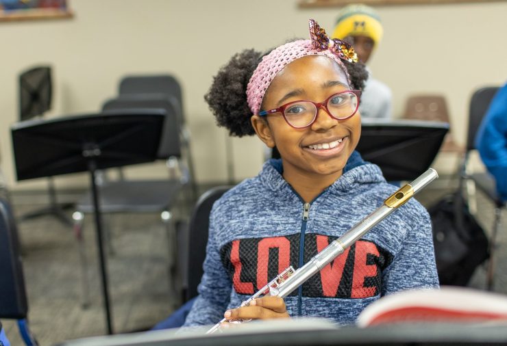 Small girl with glasses holds flute and smiles