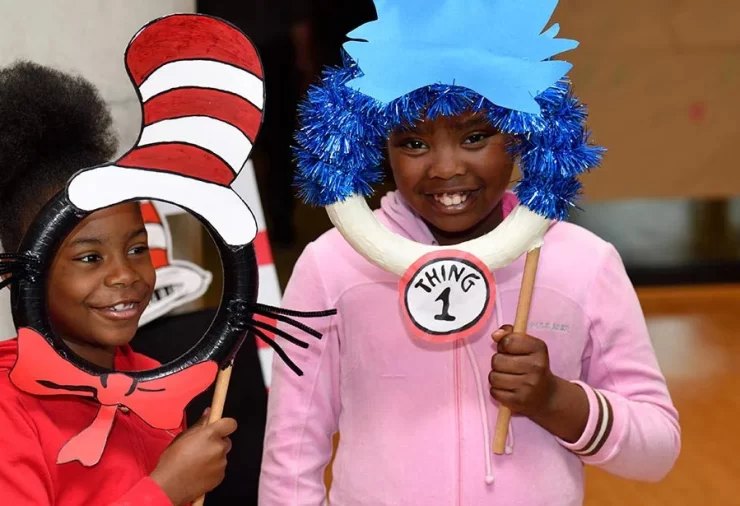 Two young girls hold up Cat in the Hat masks in front of their faces