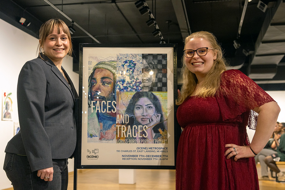 Two students stand on either side of a sign that has portrait drawings and the words: 