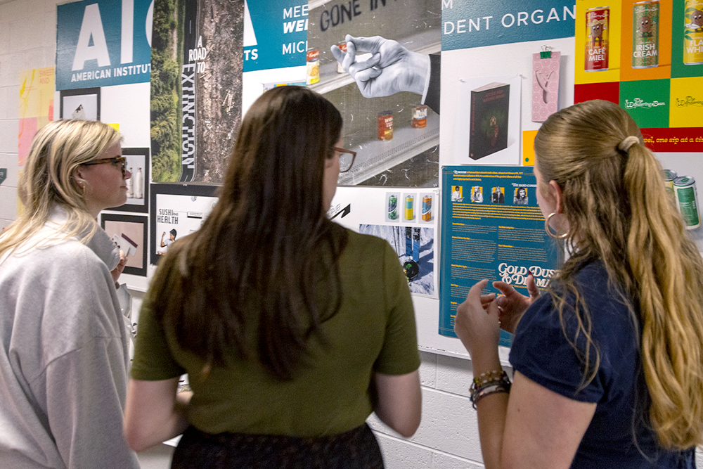 The backs of three people looking at colorful design and poster work displayed on a wall.