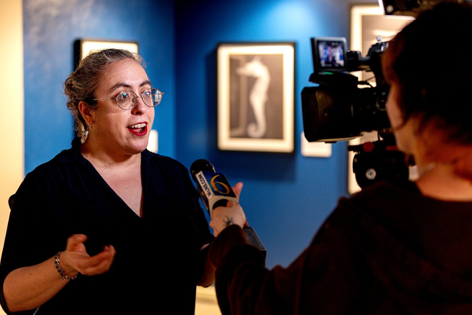 Museum Studies Professor Suzanne Fischer is interviewed by a television news reporter inside the exhibition gallery, speaking in front of museum displays during media coverage of the student-curated exhibition.
