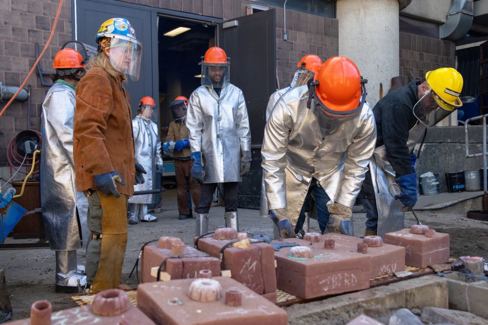 A group of people in helmets and safety jackets arrange molds before the start of an iron pour.